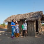 A group of people standing outside a hut Description automatically generated with medium confidence